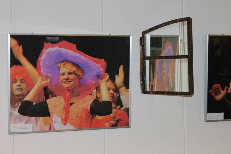 Auf einem Foto an der Wand ist ein Mädchen zu sehen, das einen großen, bunten Hut auf dem Kopf trägt. Das Mädchen lächelt.